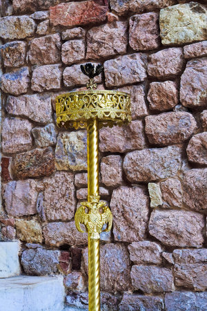A golden candle holder with the double-headed eagle symbol of the Byzantine Empire outside a stone brick wall.の写真素材