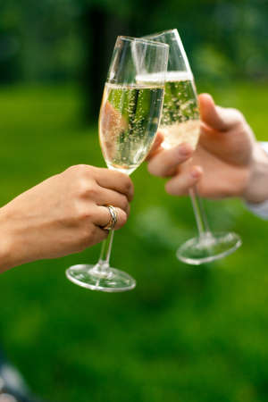 Glasses of champagne in hands on the park backgroundの写真素材