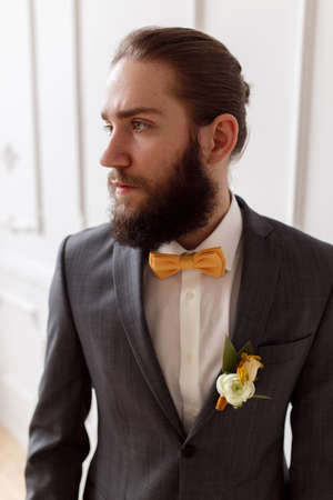 Handsome strong, brutal bearded groom posing in suit with orange bow on a light backgroundの写真素材
