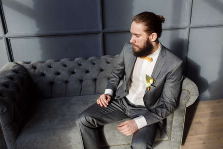 Handsome strong, brutal bearded man sitting on the grey sofa in roomの写真素材