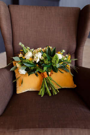 Bridal bouquet. The bride's bouquet. Beautiful bouquet of white peonies, cream roses and greenery, decorated with orange silk ribbon, lies on the orange cushions background in brown chairの写真素材