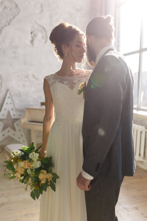 portrait of a beautiful bride with a bouquet and groom with a beard in hotel roomの写真素材