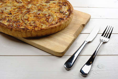 Tasty pie on a wooden board with cutlery laying on a white tableの写真素材