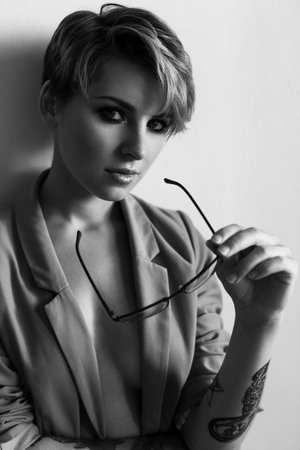 Fashion portrait of a girl with short hair wearing a jacket with glasses in hand. Black and white...