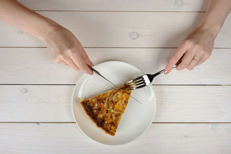 Female hands cutting a tasty piece of pie on a white plate. Top viewの写真素材