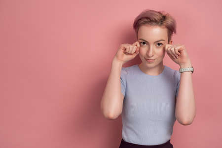 Pink-haired young woman wipes fake tears, pink backgroundの写真素材