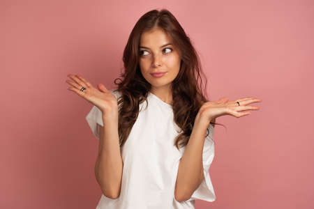 Young brunette in a white t-shirt throws up her hands as she does not know anything, pink backgroundの写真素材