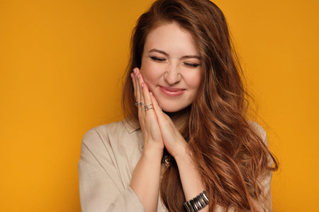 Young woman with long hair squints from happiness and enjoyment, yellow background