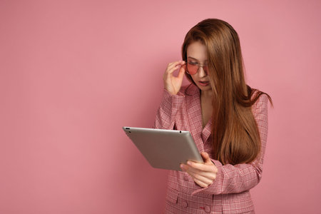 Young woman looks at her gadget through pink eye glasses over pink background