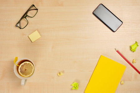 A yellow notebook with a red pencil, a cup of tea, a telephone, crumpled sheets and glasses lie on a...