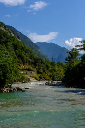 Mountain river among the greenery. White clouds in the blue sky over the mountains.の写真素材
