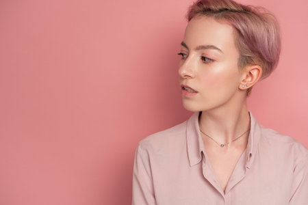 Portrait of a girl with short pink hair in a blouse and a skirt standing on a pink background in...
