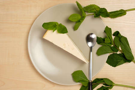 Cheesecake on a plate is surrounded by herbs on a light wooden tableの写真素材