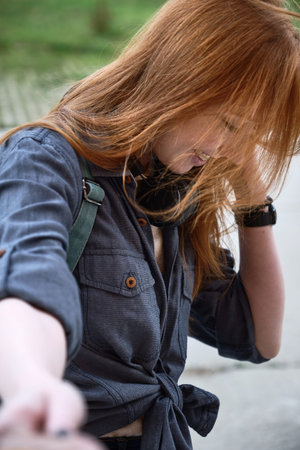 Red-haired girl in a blue shirt with headphones on her neck, laughing head down, holding out his...