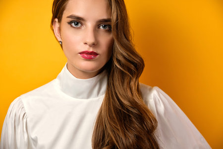 Close portrait of a beautiful girl with curls and red lipstick in a white blouse against a yellow...