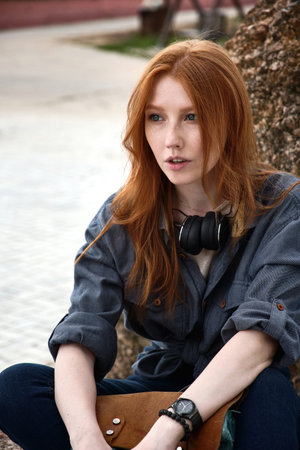 A close portrait of a red-haired girl with freckles and blue eyes, with headphones on her neck in a...