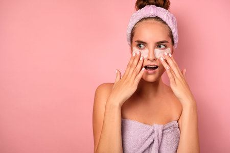 A girl in a lilac towel with collected hair stands with patches under her eyes and frightenedly...