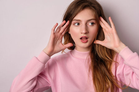 The girl in pink t-shirt standing on a light background, surprised mouth open, keeps your hands up...