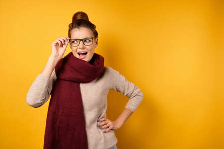 A beautiful brunette with gathered hair in a burgundy scarf looks with astonishment to the side, adjusting her glasses.の写真素材
