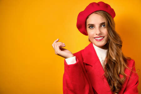 A beautiful girl with red lips stands in a red coat and takes on a yellow background and wets frame.の写真素材