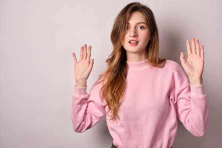The girl in pink t-shirt standing on a light background, surprised mouth open looking at the camera, holding up his hands.の写真素材