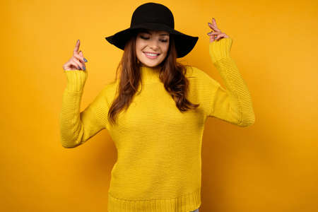 A brunette is standing on a yellow background in a yellow sweater and black hat and is dancing and smiling.の写真素材