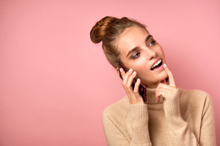 A girl in a turtleneck with a high bun on her head thoughtfully speaks on the phone with her head...