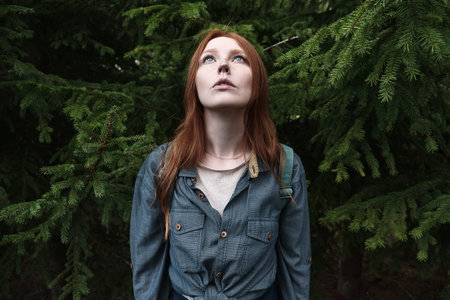 A redhead girl with blue eyes in a denim shirt stands straight and looks up holding her head against...