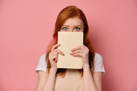 A red-haired girl in a beige apron and a T-shirt stands on a pink background and opens her eyes wide...