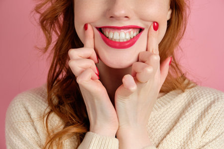 A close shot of the face of a red-haired girl with red manicure and lipstick, stretching a smile...