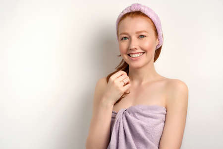 Redhead girl with clean skin in a towel and a bandage on her head smiles broadly at the cameraの写真素材