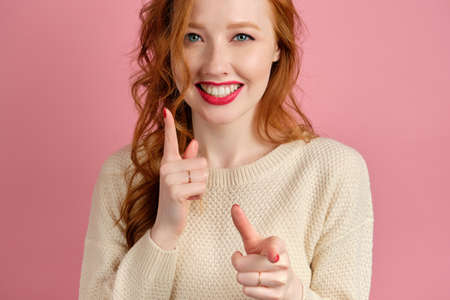 The red-haired girl with red lipstick smiles broadly and holds her hands in front of her with index fingers forwardの写真素材