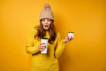 A beautiful brunette in a yellow sweater and hat stands on a yellow backgroundの写真素材
