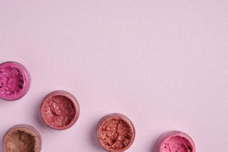 Lipsticks are in round jars in the corner of the frame on a lilac backgroundの写真素材