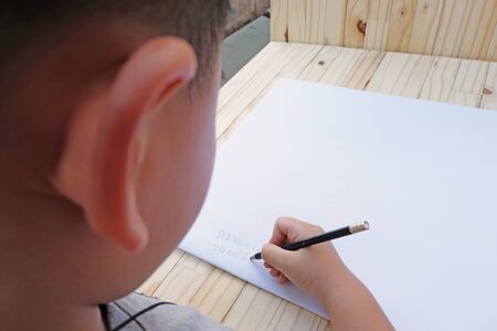the rear view of a boy writing alphabets by his right handの写真素材