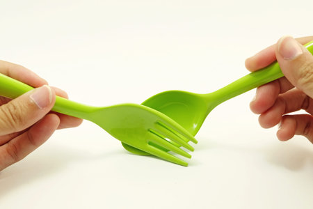 green plastic spoon and fork are held by both hand and pretending to scoop food with yellowish white backgroundの写真素材