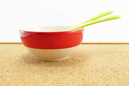 side view green plastic spoon and fork in a red bowl on cork plywood boardの写真素材