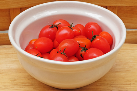 The Tomato pile with some water drop on a white bowl and wooden backgroundの写真素材