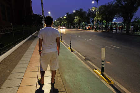 Backside of Man who stands on street corridor and looks forward to the road and some vehicles at nightの写真素材