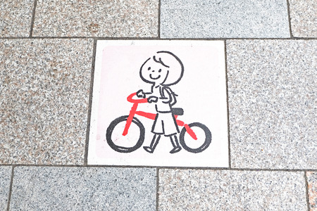 "a girl cartoon hands and walk with a red bicycle" plate sign on the pathway groundの写真素材