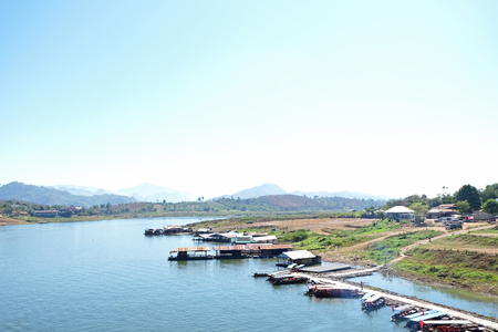 small dock and many ships in the river with mountains and light blue sky at Mon Bridge Public Sightseeing in Kanchanaburi,Thailandの写真素材
