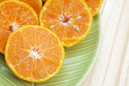 center (Selected focus) of orange half which is at left below side of frame and other oranges on light green plate on wood groundの写真素材
