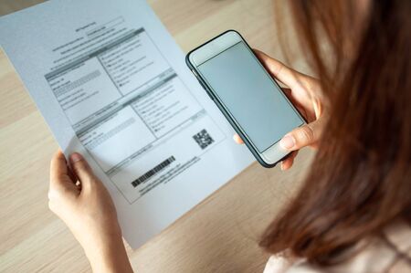A woman uses a smartphone to scan the barcode to pay monthly phone bills after receiving an invoice sent to home. Online bill payment conceptの写真素材