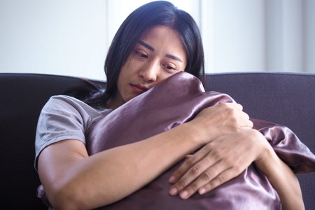An Asian woman with mental pain is sitting alone hugging a pillow.