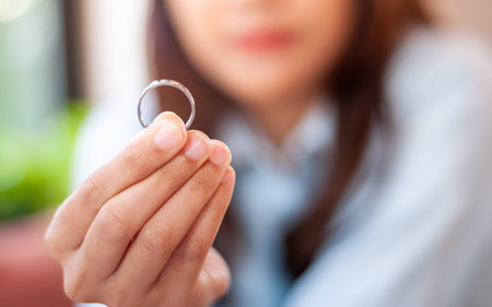 Close up of a single sad wife after divorce lamenting holding the wedding ring in a house interior.