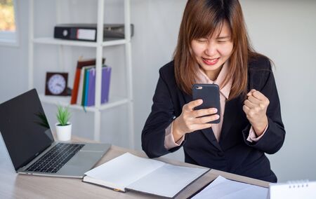 An Asian businesswoman looks happy while looking at the information on the phone.の写真素材