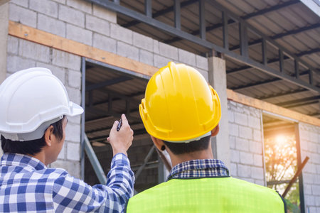Two men on construction site wearing hard hats. Standing and talking about the problems of house...