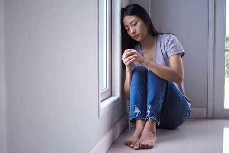 An Asian woman was sadly sitting by the window in the room. Feeling sad and lonely.の写真素材