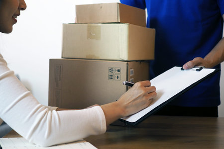 The shopper girl signs on the clipboard to receive the package box from the delivery man. Fast...