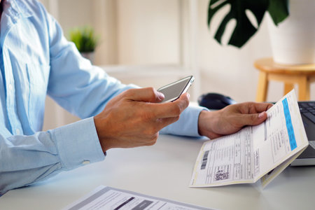 The image of a man's hand holding a smartphone and bill. Pay online via the application